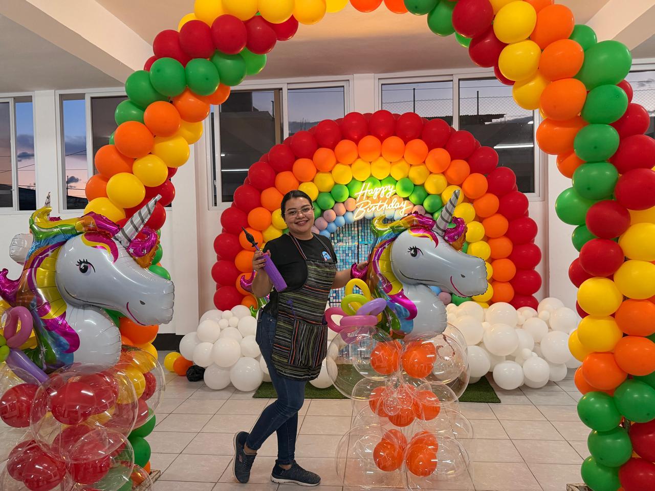 Decoradora con un inflador frente a un arco arcoíris con globos de unicornio.