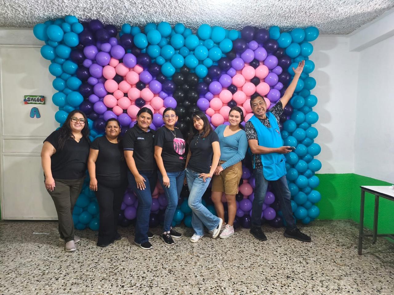Equipo de decoradores frente a un muro de globos turquesa, morados y rosados recién montado.