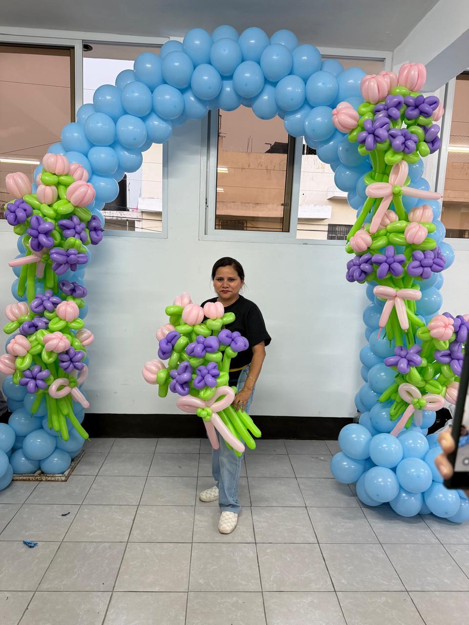 Decoradora sostiene un ramo de flores de globo frente a un arco celeste.